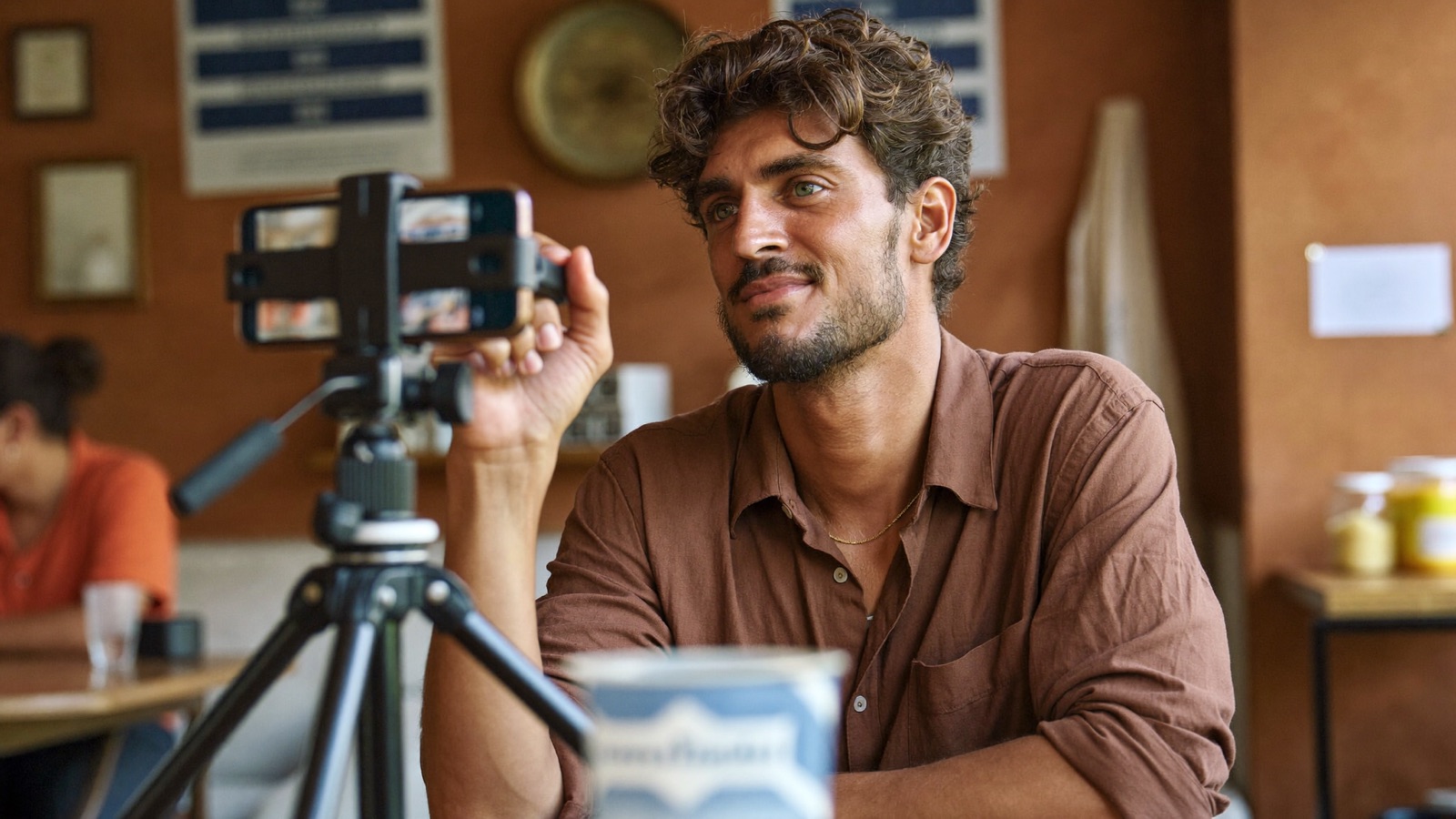 A cafe owner films a short social video on a phone tripod at his counter