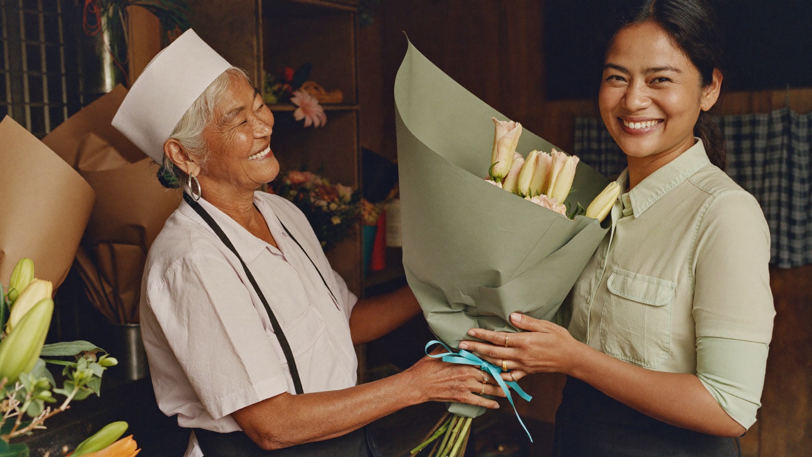 A florist warmly hands a wrapped bouquet to a returning regular customer