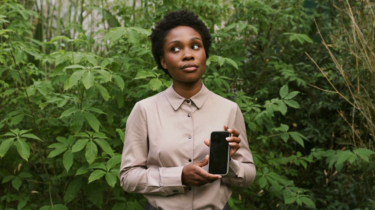 A small business owner holding up her phone with a skeptical expression, checking her listings