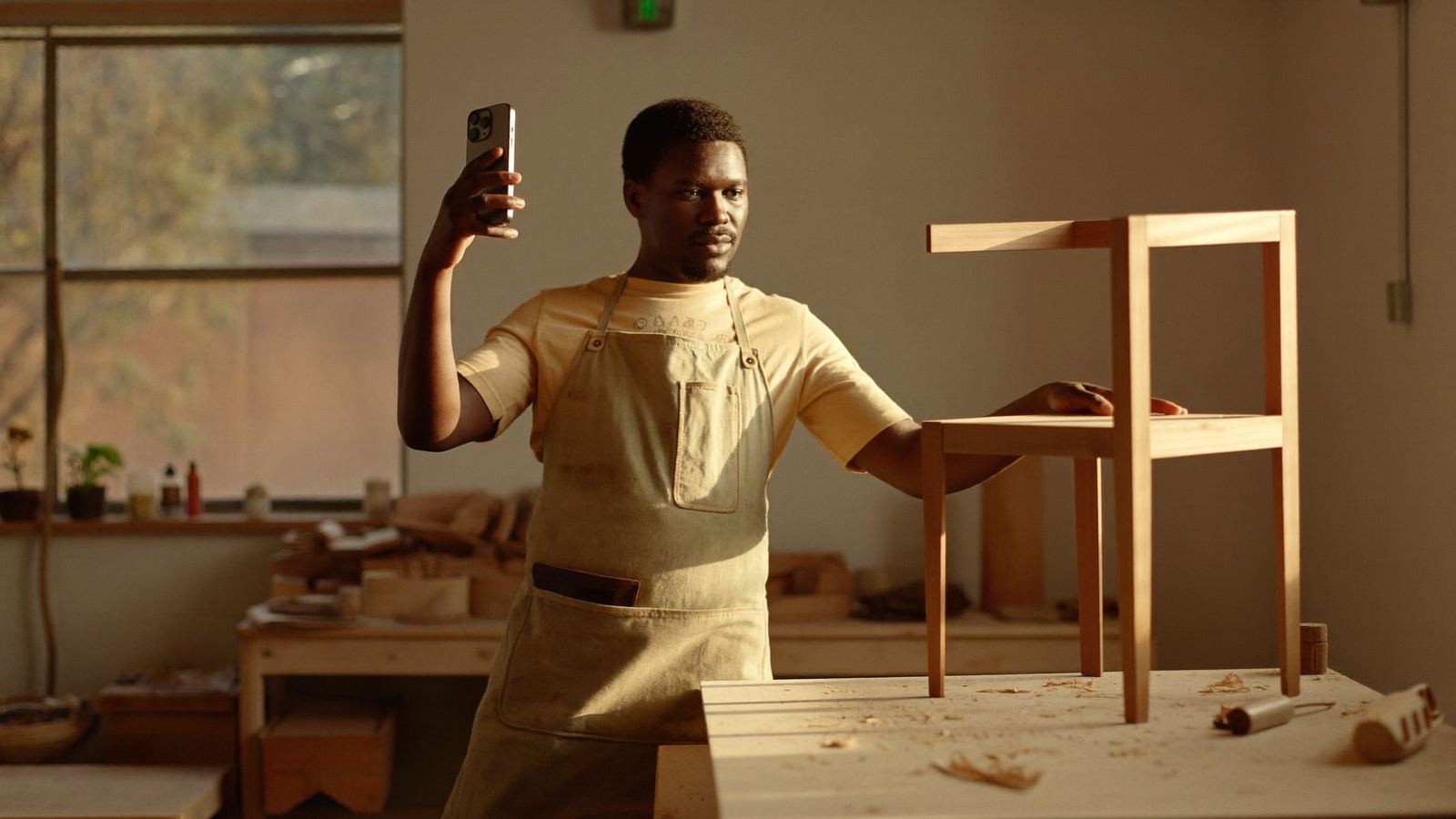 A woodworking shop owner films a short video of a finished chair on his phone for a shoppable post
